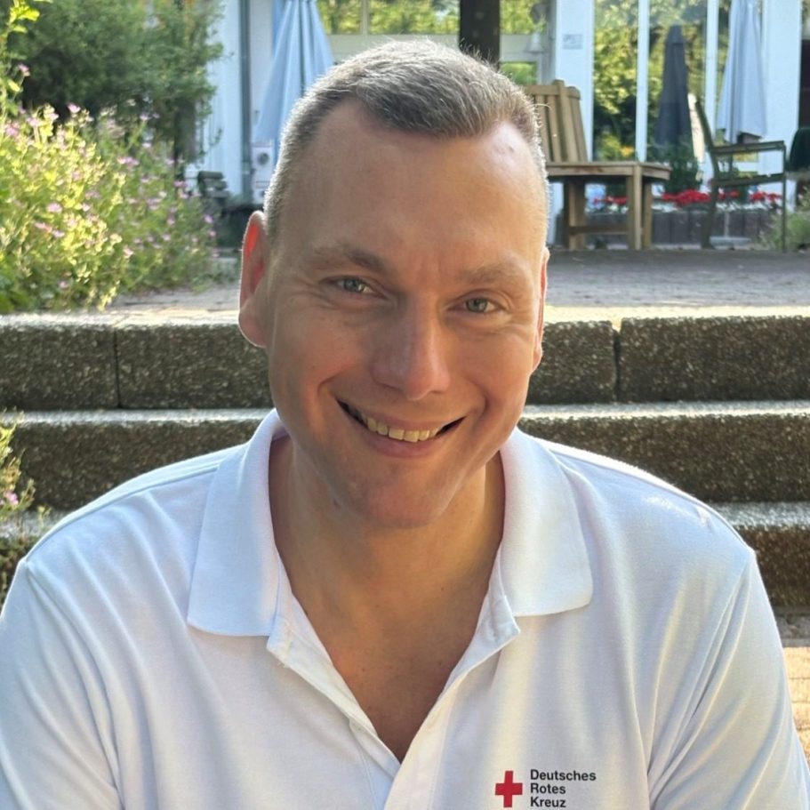 Eric Winkler - Geschäftsführer Heinrich-Gerold-Haus Lächelnder Mann in blauer Polo-Uniform vor grünem Hintergrund.