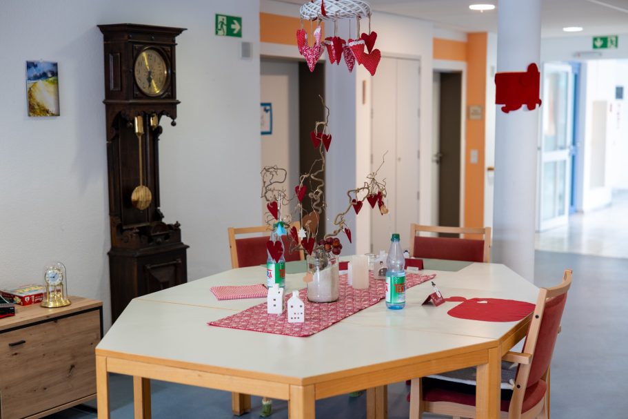 Heinrich-Gerold-Haus DRK - Pflegeheim in Ober-Ramstadt Ein Essbereich mit einem achtkantigen Tisch, roten Dekorationen und einer Wanduhr.