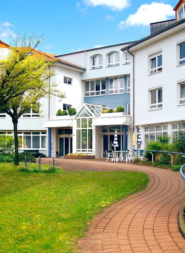 Heinrich-Gerold-Haus DRK - Pflegeheim in Ober-Ramstadt Moderne Wohngebäude mit Garten und geschwungener Gehweg. Heller Himmel im Hintergrund.