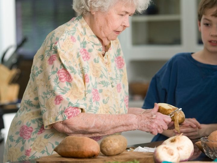 Pflege - Heinrich-Gerold-Haus Eine ältere Frau schält Kartoffeln, während ein Junge ihr zusieht.